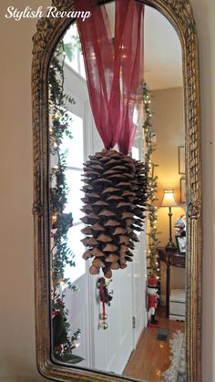 a mirror that has some pine cones hanging from it's side and is decorated with red ribbon