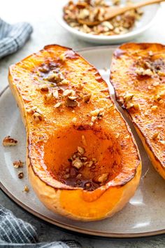 two slices of baked sweet potatoes on a plate with nuts and seasoning in the background