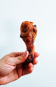 a hand holding up a piece of food that looks like a chicken leg with meat on it