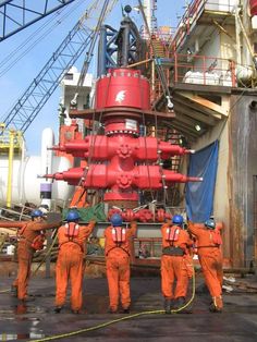 three men in orange work on an oil rig