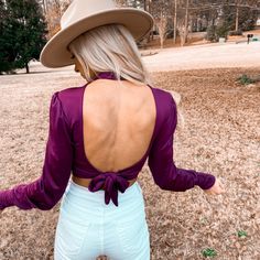 Woman outdoors fa ring backwards showing a purple open-back top while wearing a hat. Spring Purple Satin Top, Purple Satin Top For Spring, Chic Purple Long Sleeve Crop Top, Chic Long Sleeve Purple Crop Top, Fitted Purple Crop Top For Fall, Purple Crop Top For Spring Night Out, Purple Satin Party Top, Chic Purple Crop Top For Party, Silk Bodysuit