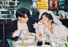 two people sitting at a table with bowls of food and chopsticks in front of them