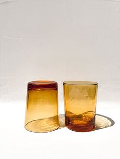 two yellow glass cups sitting next to each other on a white tableclothed surface