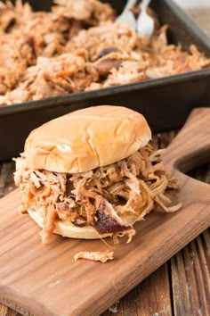 a pulled pork sandwich sitting on top of a wooden cutting board next to a pan