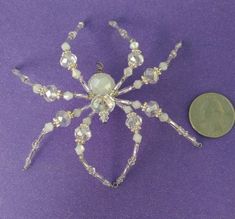 a silver spider brooch sitting next to a penny on a purple surface with a white background