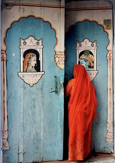 a woman in an orange sari is standing at the entrance to a blue door