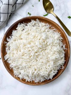 white rice in a wooden bowl next to a spoon and napkin on a marble counter