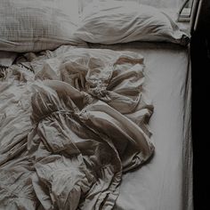 an unmade bed with several pillows and blankets on top of it, in black and white