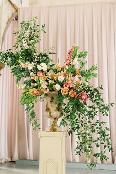 a vase filled with lots of flowers sitting on top of a table next to a plant