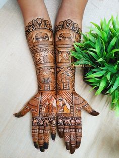 two hands with henna designs on them next to a potted plant and green leaves