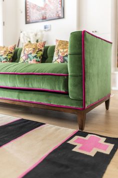 a green couch sitting on top of a hard wood floor next to a colorful rug