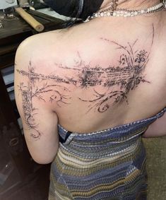 the back of a woman's shoulder with an artistic tattoo design on her left side