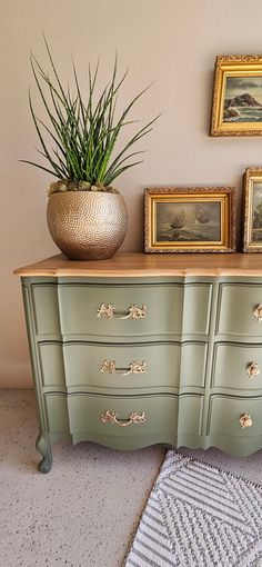 a green dresser with some pictures on the wall and a potted plant next to it