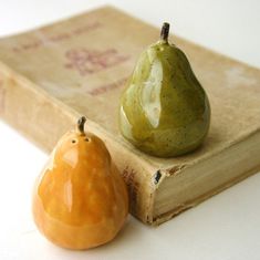 two small figurines sitting on top of an old book next to a pear