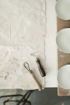 the table is set with white plates and utensils on it, along with a rolling pin