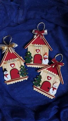 three small wooden houses with snowmen and christmas trees on them sitting on a blue cloth