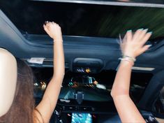 two women in the back seat of a car with their hands up to the ceiling