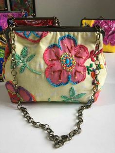 a small purse with flowers and chains hanging from it's front pocket, sitting on a table