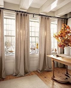 a living room filled with lots of windows covered in curtains and drapes next to a wooden table