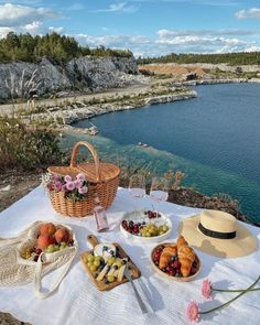 a picnic table with fruit, cheese and bread on it next to the water's edge