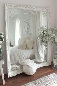 a large white mirror sitting on top of a wooden floor next to a vase filled with flowers