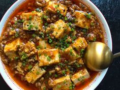 a white bowl filled with tofu and some green onions next to a golden spoon