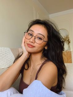 a woman wearing glasses sitting on a couch with her hand under her chin and looking at the camera