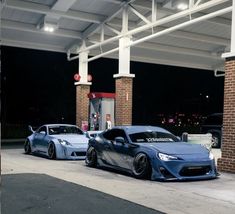 two blue sports cars parked in front of a gas station