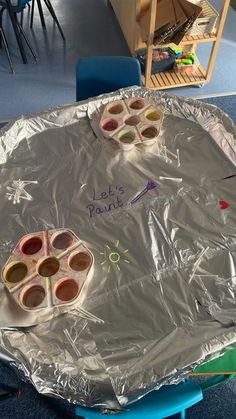 there is a tin foil covered table with cups and paintbrushes on it that says let's paint