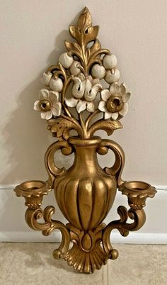 a gold vase with flowers and candles on the wall next to a white tile floor