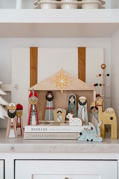 a nativity scene is displayed on top of some books in a white shelf next to a christmas tree