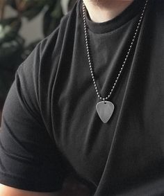 a man wearing a black t - shirt with a heart shaped pendant on his neck