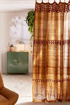 a brown chair sitting next to a window covered in sheer curtaines and a potted plant