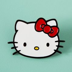 a hello kitty pin sitting on top of a green surface with a red bow in it's hair