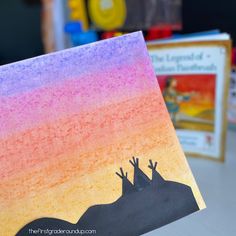 a hand holding up a colorful card with two giraffes painted on it