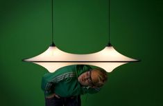 a man is standing in front of a green wall with three lights hanging from it