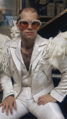 a man in white suit and sunglasses sitting next to a piano