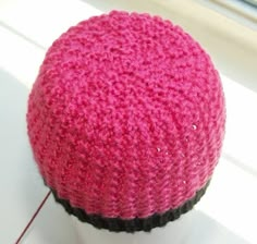 a knitted pink and black hat sitting on top of a white mannequin