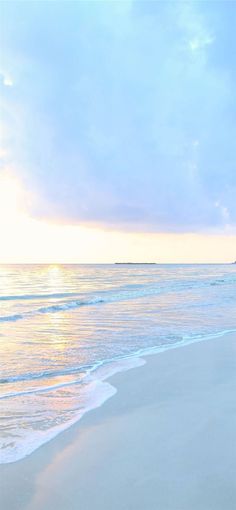 the surfboard is laying on the beach near the water's edge as the sun sets