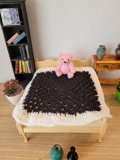 a pink teddy bear sitting on top of a black and white crocheted blanket