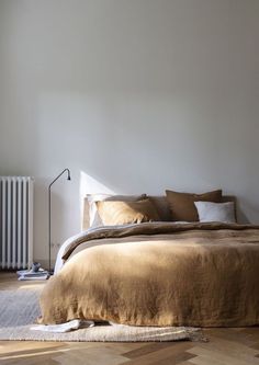 a large bed sitting next to a radiator in a white room with wooden floors