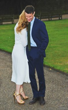 a man and woman standing next to each other in front of a grass covered field