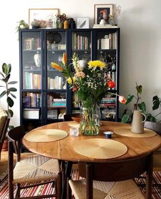 a wooden table with chairs around it in front of a bookcase filled with books