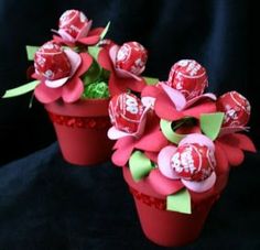 two red vases with candy in them on a black cloth covered surface, one has flowers and the other has hearts