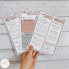 two hands holding up three newish class news cards on top of a wooden table