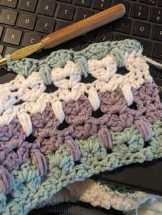 a crocheted blanket sitting on top of a laptop computer next to a keyboard