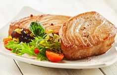 a white plate topped with meat and salad on top of a wooden table next to a fork