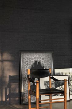 a black chair sitting in front of a brick wall with pictures on the floor next to it