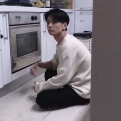 a young man sitting on the floor in front of an oven