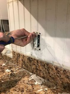 a man is fixing an electrical outlet on the wall in his kitchen with marble countertops